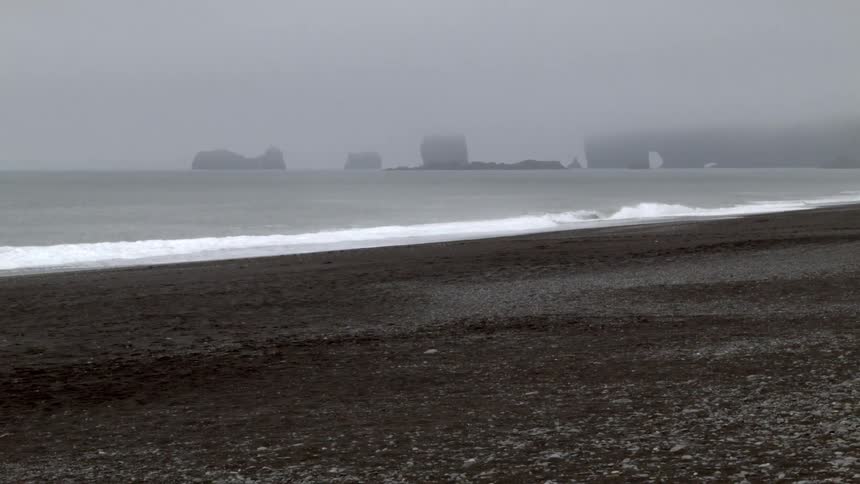 Waves crash against the shore on a foggy day