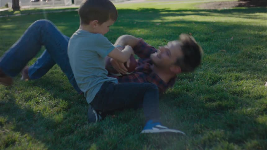 Father lying down with his son playing on the grass in a park