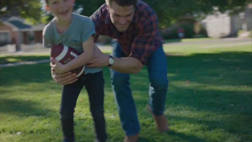 A boy running with a ball and playing with his father who hugs him