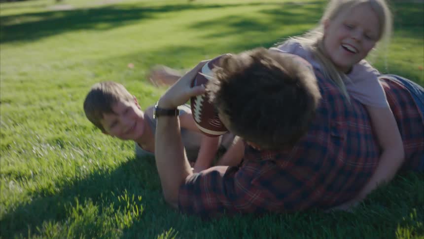 Father and his children playing with a ball on the grass outdoor at midday
