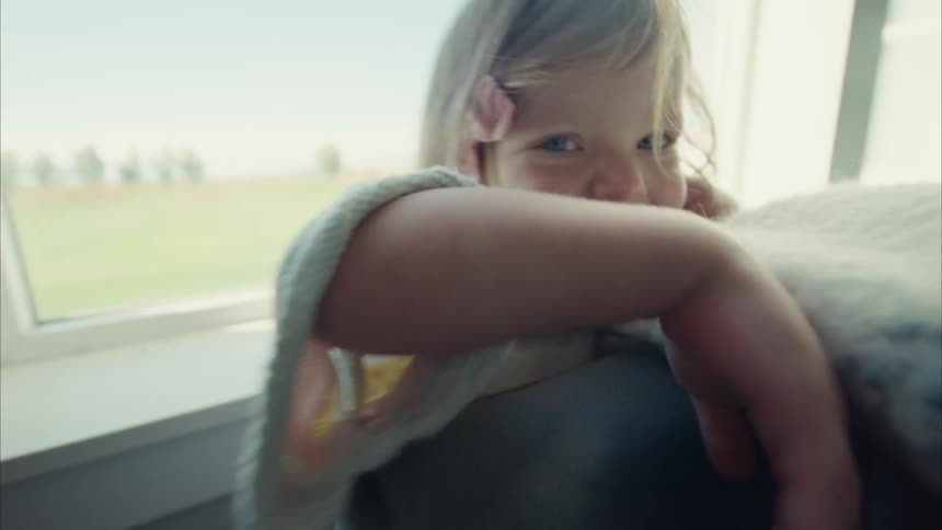 Portrait of a little blonde girl playing hideandseek behind a sofa