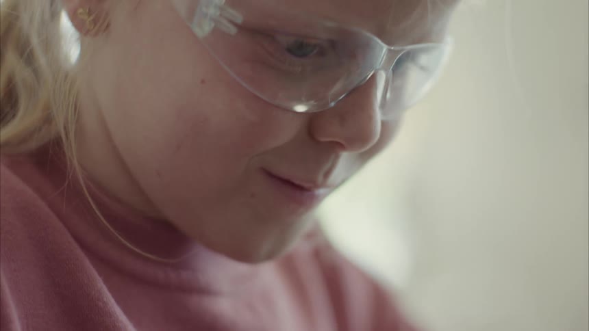 A girl wearing protective glasses smiles while touching something