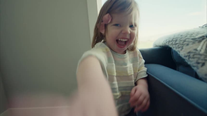 A young girl laughing and running across a living room