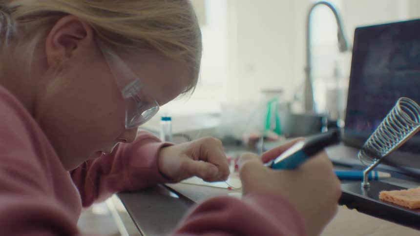 Focused girl using a soldering tool on a hardware board