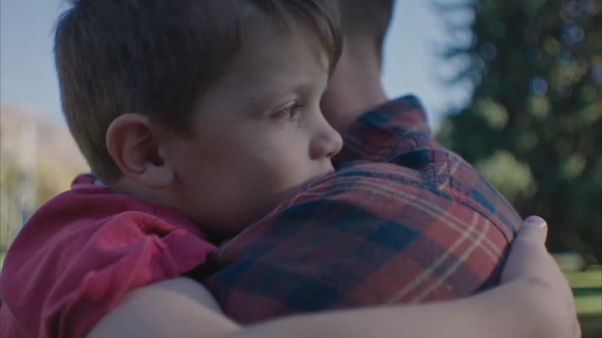 A boy on his fathers lap hugging himself
