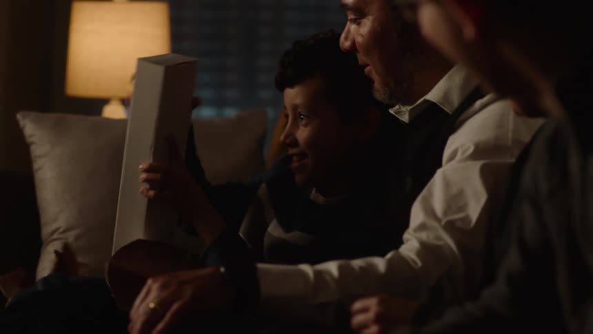 Boy opens a present sitting with his father in the couch