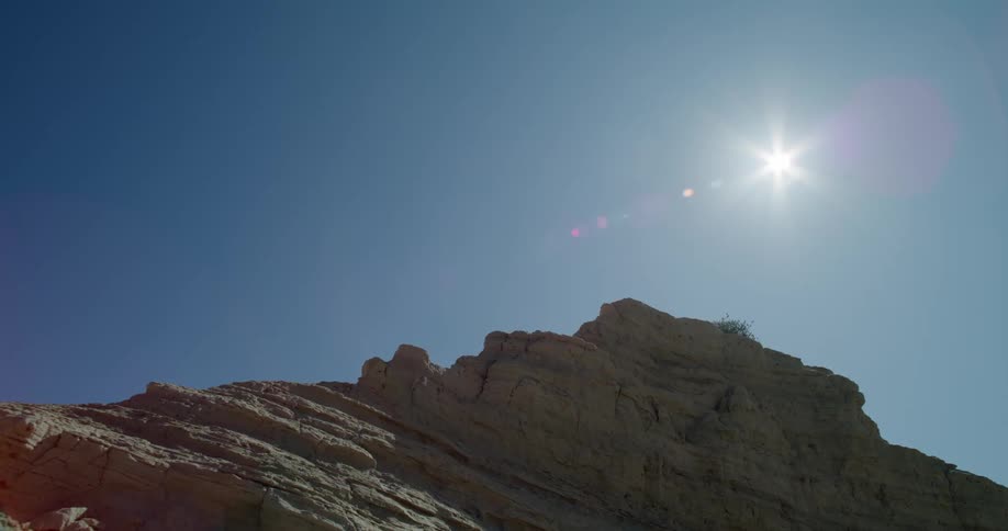 The sun shines brightly in a blue sky over a rocky mountain