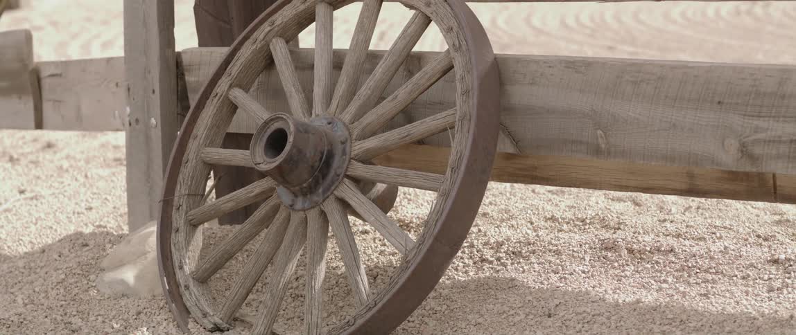 A wagon wheel is leaning against the fence