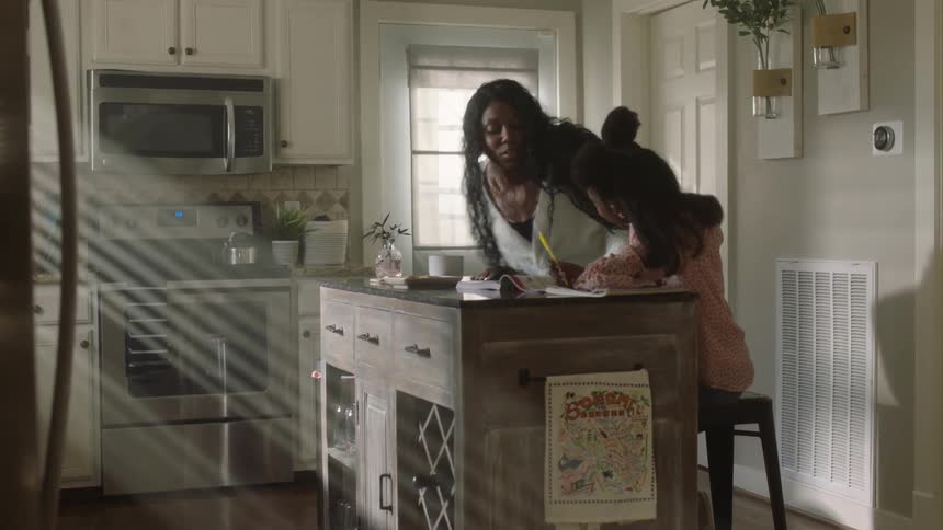 Mother sitting next to her daughter who is studying in the kitchen