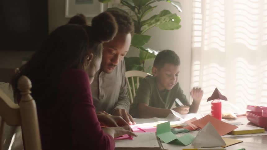 A family of one adult and two children playing with papers on a table
