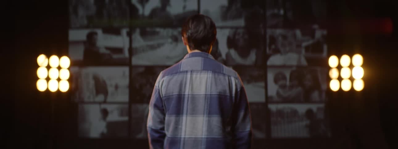 A man facing a big screen displaying various videos