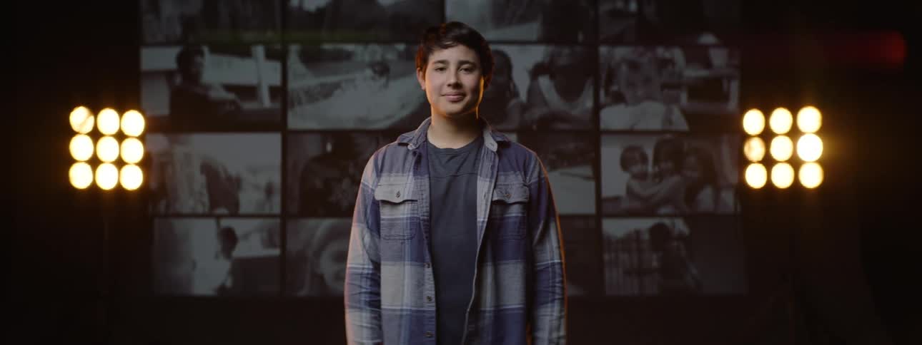 Teen smiles while standing in front of a big screen in a dark room