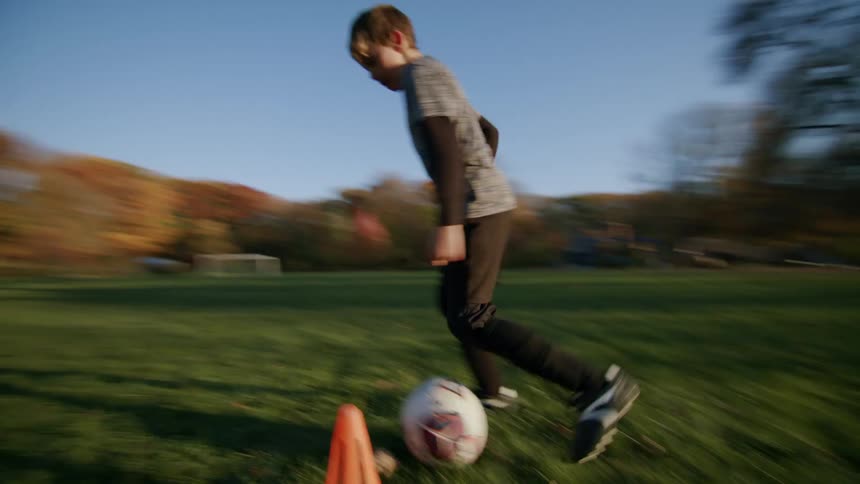 A kid training with a soccer ball by going around cones