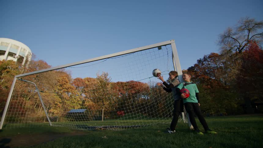 Two young friends holding a soccer ball next to the goalpost on a field