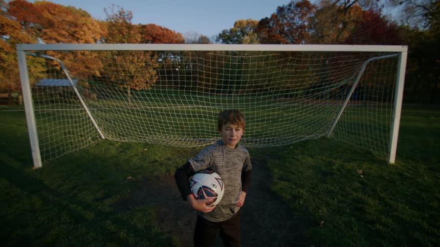 A boy with a soccer ball in his arms in front of the goal