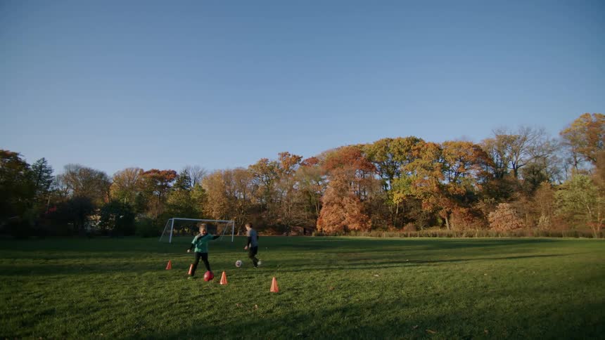 Two boys are running with a soccer ball past obstacles on the lawn