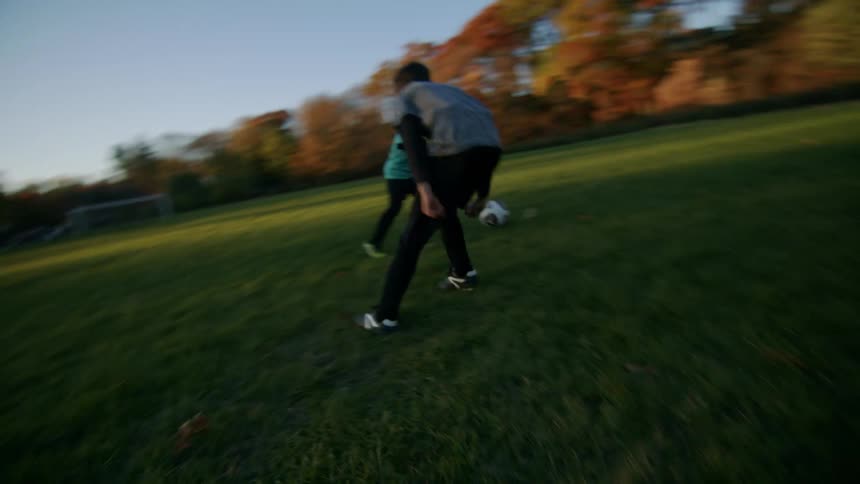 Brothers play with soccer ball on soccer field near apartment buildings during the fall