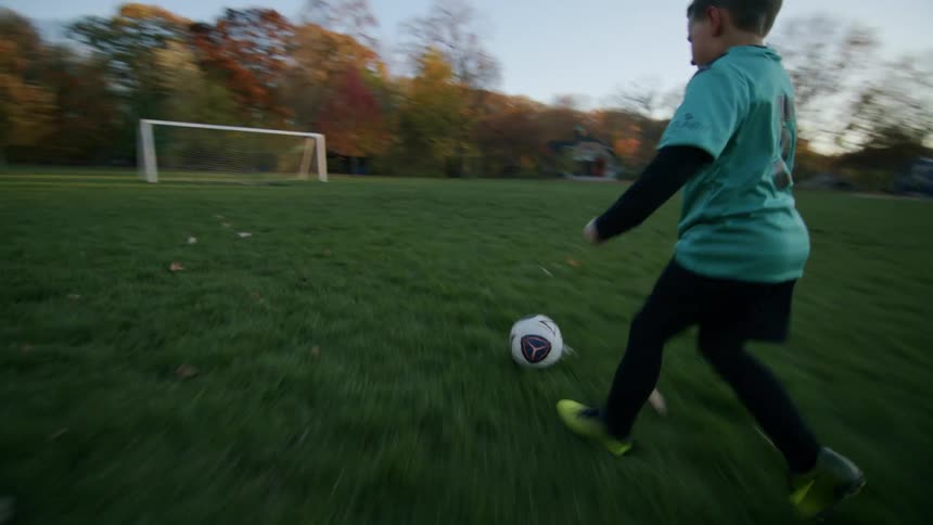 The boy gets up runs after the ball and kicks scoring a goal