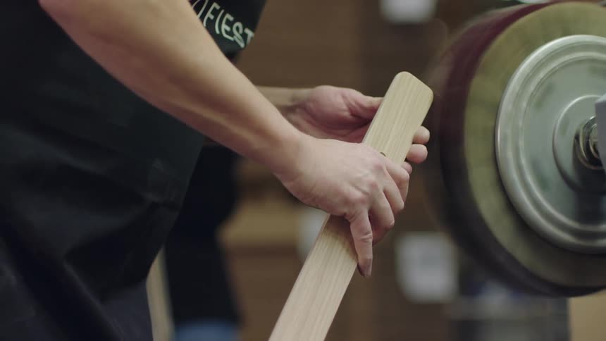 A woodworker uses a powered tool to smooth a curved piece of wood