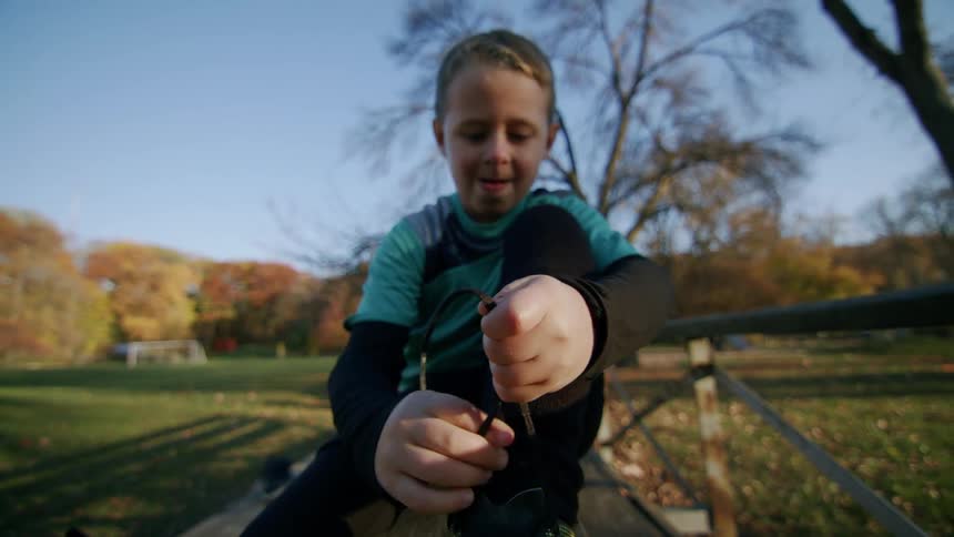 A child knotting his soccer boot while sitting down