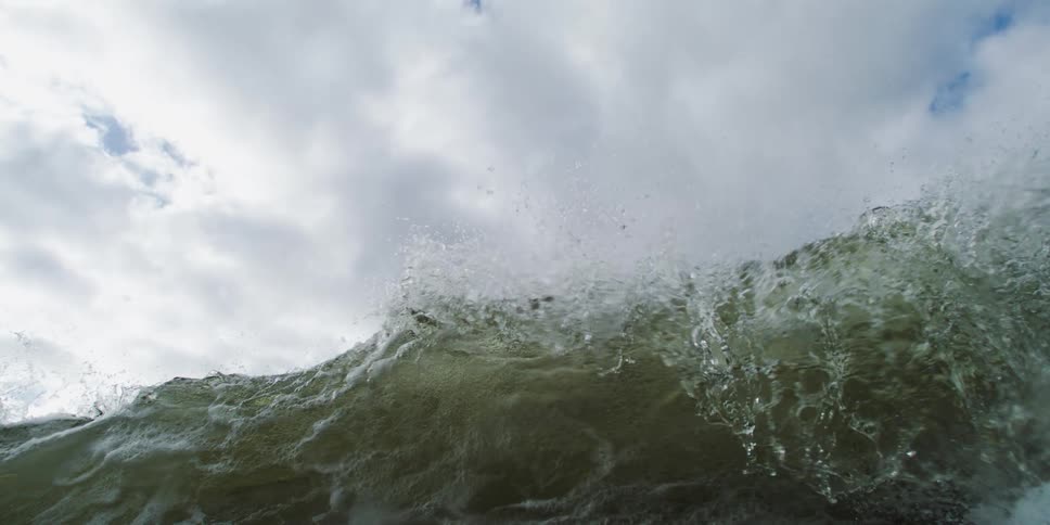 Ocean wave crests and collapses under a cloudy sky