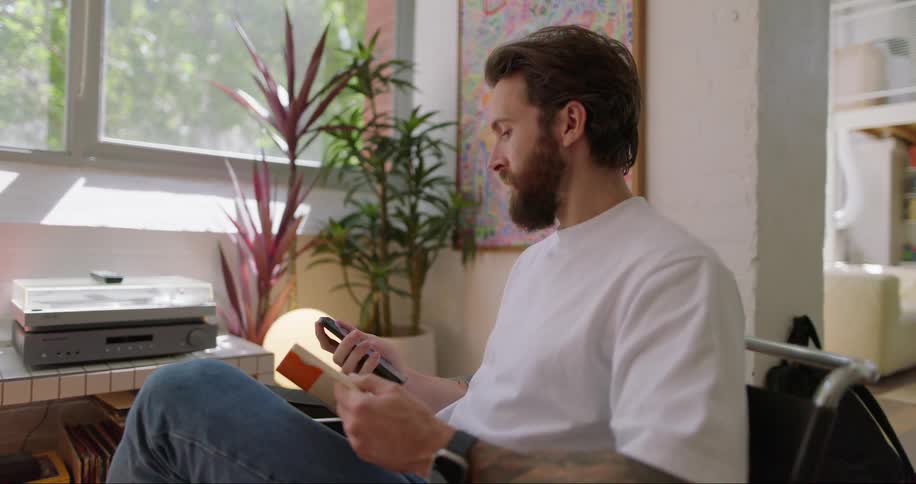 Man sitting indoor reads a book after texting on mobile phone