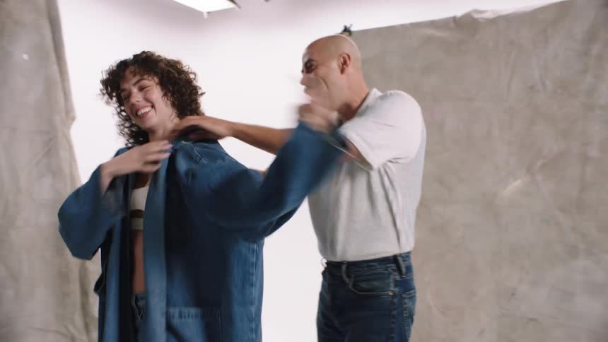 Man picking up a denim jacket and putting it on the model in a studio photo white cyc studio