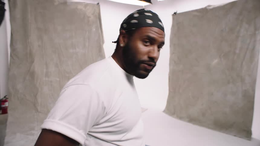 Man wipes and taps camera before sitting on stool in photography white cyc studio blue collar quirky