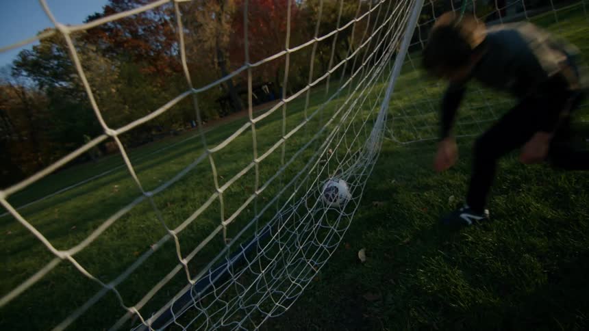 Young boy kicks and retrieves a soccer ball from net