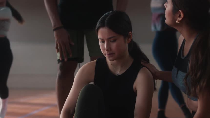 Fellow dancers gather around injured female dancer during practice