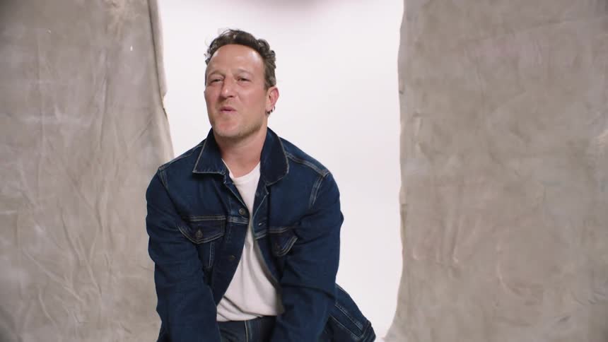 A man in denim jackets is smiling while posing sitting