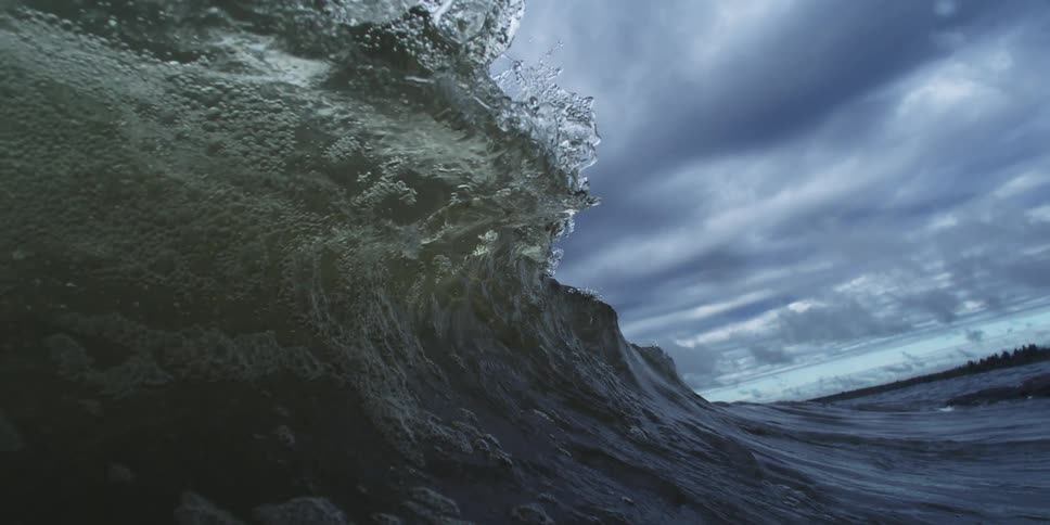 A sea wave is breaking and several drops are falling from the crest