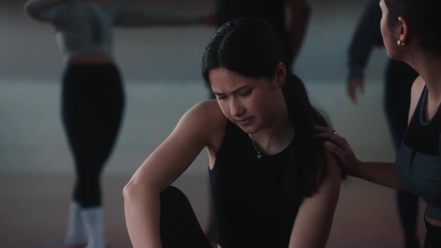 Girl in a dance class experiencing leg pain squatting in the middle of the class while her peers come to help
