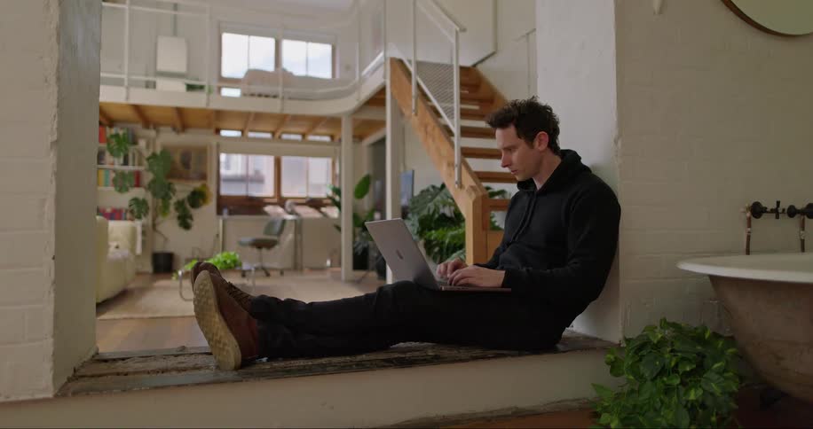 Man sitting on the floor at home typing on a laptop