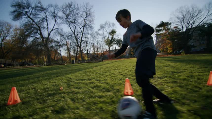 Boy dribbling around cones on a grass field