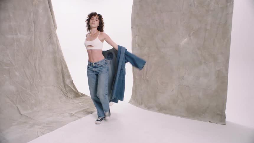 Curlyhaired woman takes off denim trench coat and spins around before putting it back on