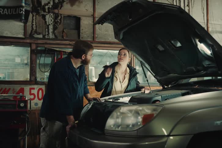Two people talking in a workshop next to a pickup truck with the car hood open