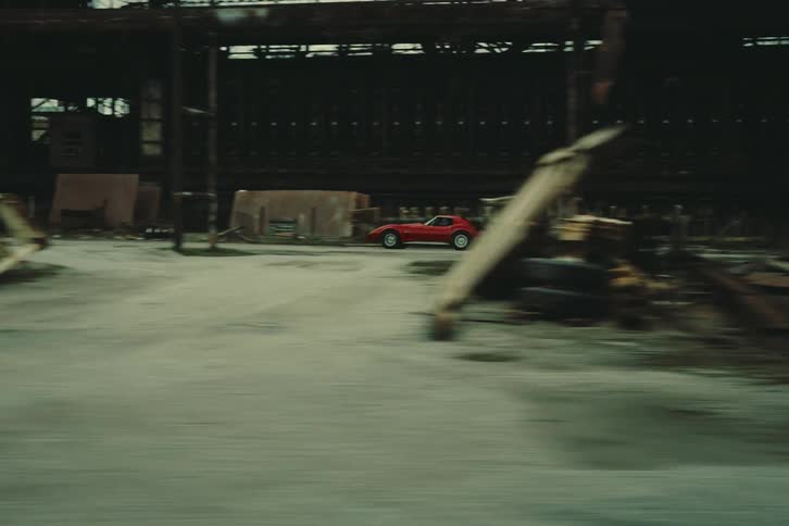 A person drives a red corvette down an industrial road on a cloudy winter day