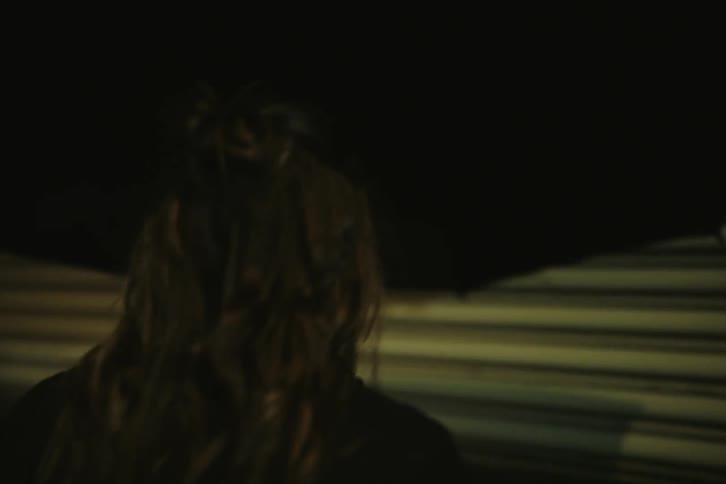 Woman walking backward on the street at night with an umbrella then opening a gate and entering a garage