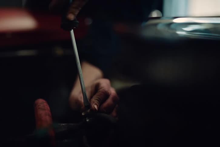 Close up of car mechanics hands using a screwdriver to fix a car