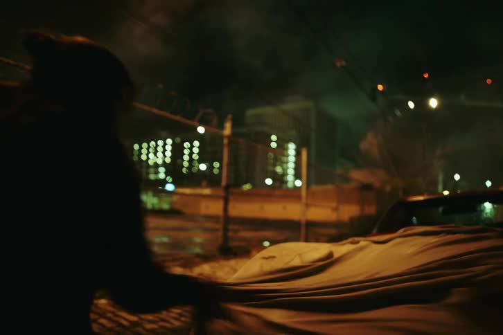 A person with a flashlight taking a sheet from a red car parked on the street at night