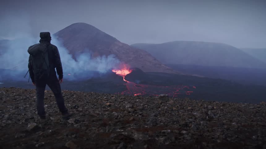I clip of a man standing and watchin a volcano erupt