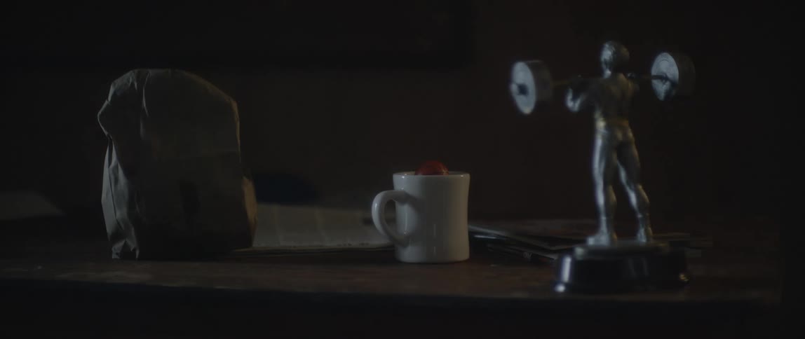A person passes by and places a handbag on a table that has a mug and a trophy