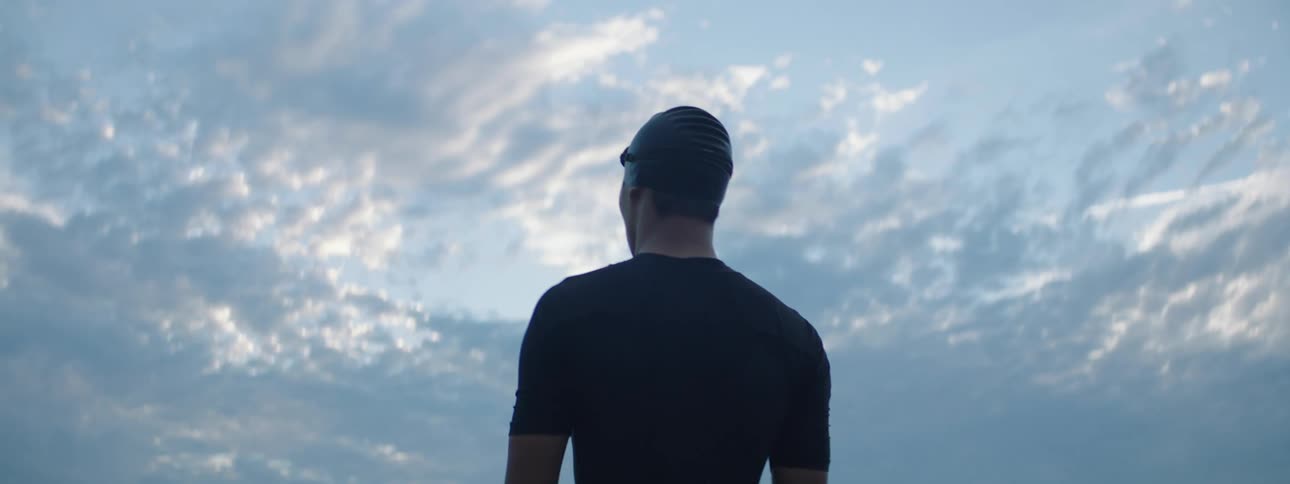 Man wearing cap stands outdoors looking around under an overcast sky