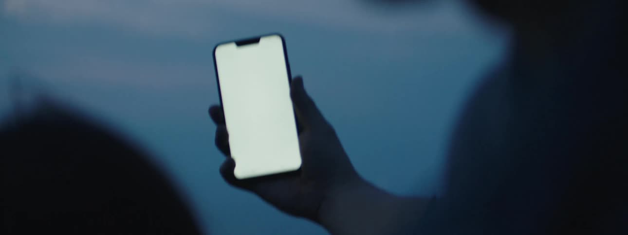 A person holding and waving at a cell phone with a completely white screen