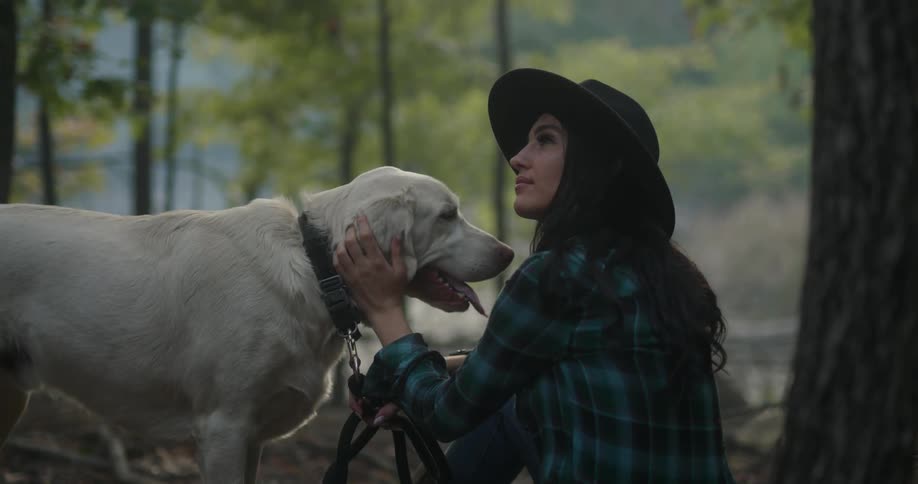 A woman is petting her dog in the forest