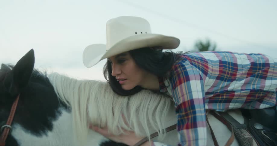 A woman riding a horse bends forward to lay her head on its neck while petting it
