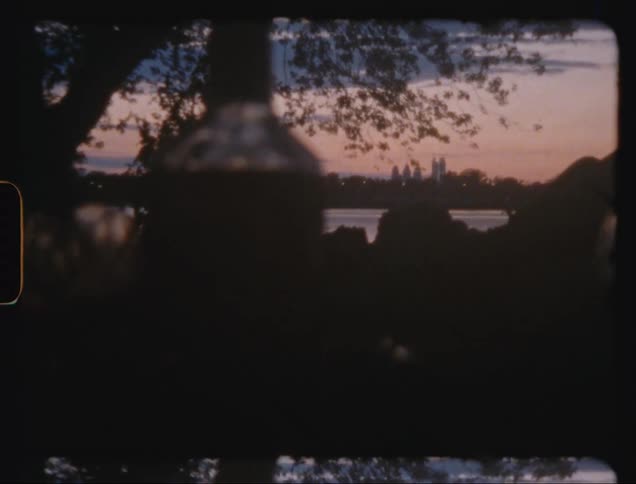 Negative zoom of a garden with a lake in the foreground and a metropolis on the horizon with skyscrapers against a reddish dawn sky