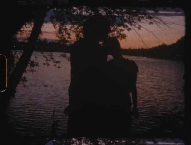 Silhouette of a couple kissing by a lake in a late afternoon sky