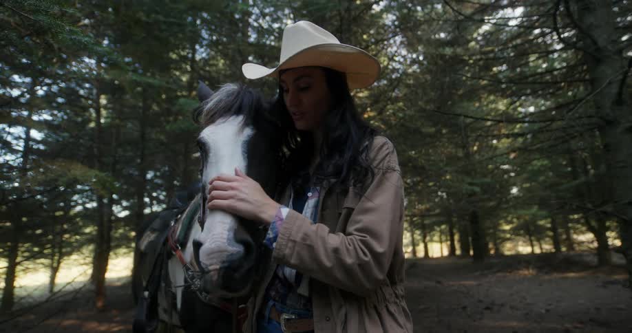 Woman with a cowboy hat petting the horses face in a forested area